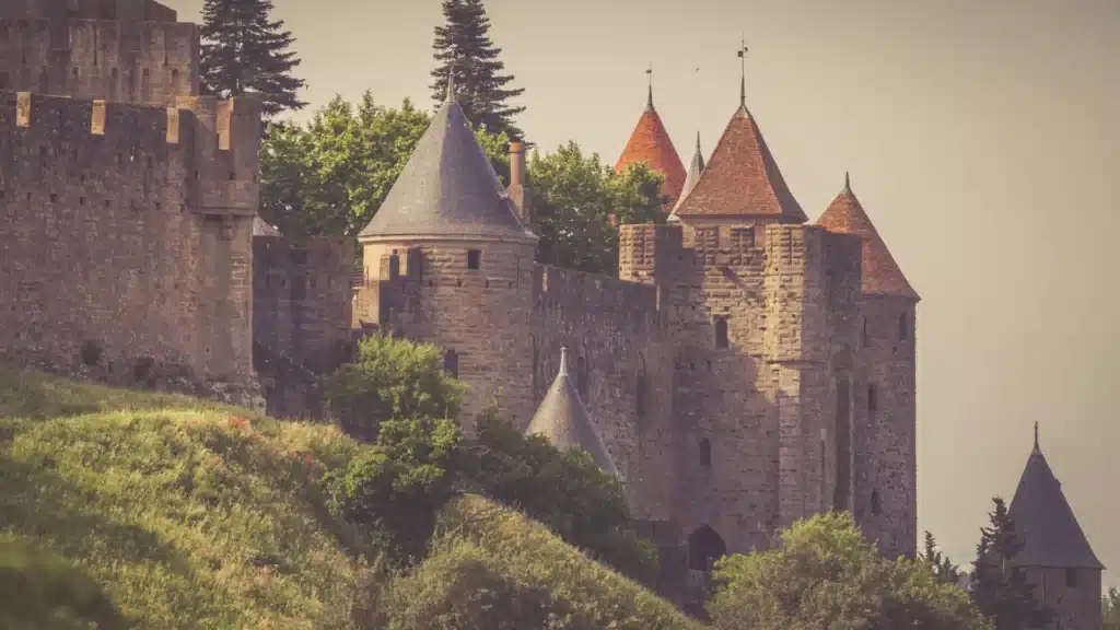Magnifique château médiéval et ses puissants remparts. Grands remparts et tours en pierre d'un château médiéval, dont une à toit rouge, juché sur une colline verdoyante.