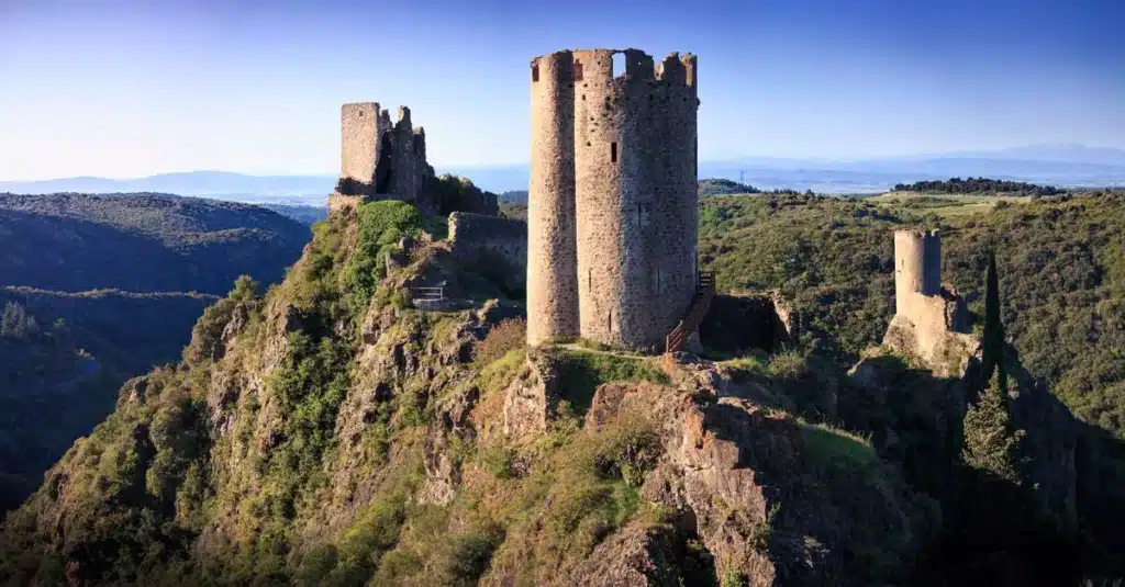 Château en ruines : forteresse médiévale sur un pic rocheux. Tours et ruines du château médiéval perchées sur un pic rocheux escarpé. Soleil sur le paysage montagneux boisé et la vallée.
