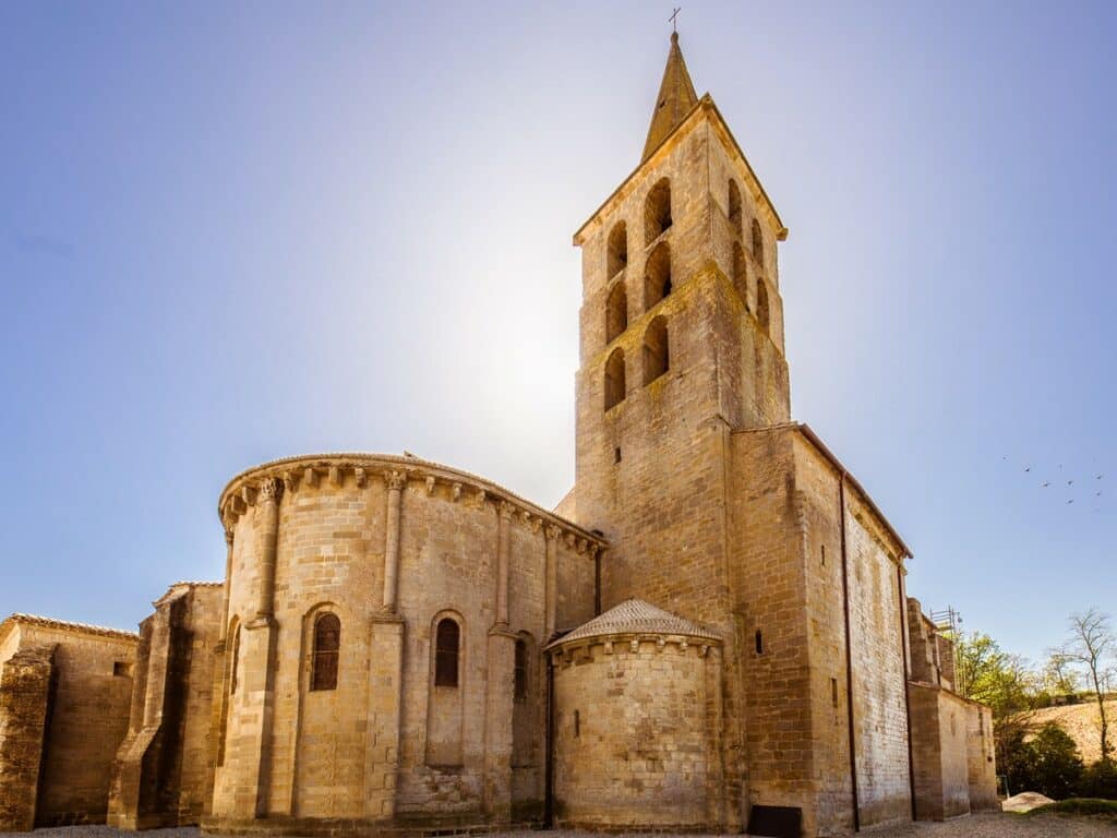 Clocher roman et chevet d'une église historique sous le soleil Façade latérale et chevet semi-circulaire d'une église romane en pierre blonde. Le haut clocher percé de baies est illuminé par le soleil.