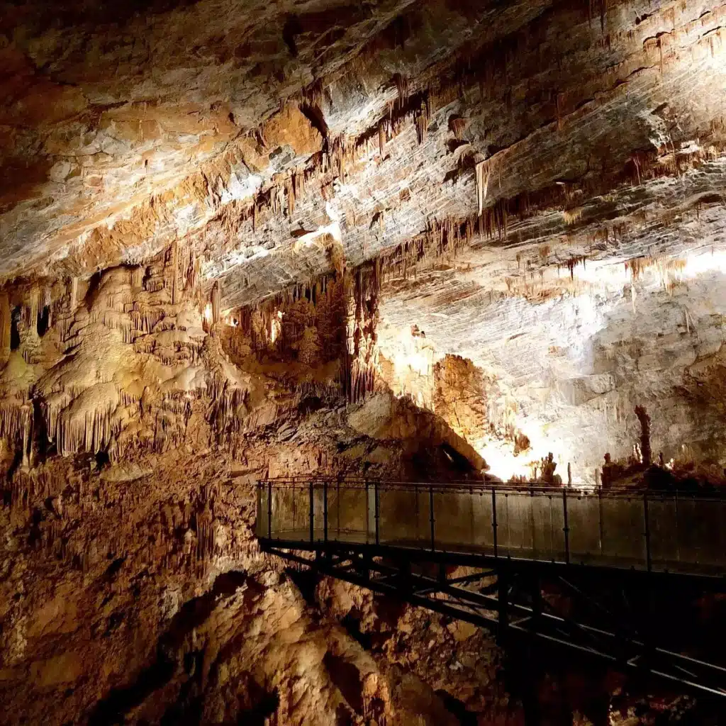 Grotte spectaculaire : Stalactites et passerelle de la caverne. Vaste caverne karstique richement illuminée. Le plafond est couvert de stalactites surplombant une passerelle touristique en métal.