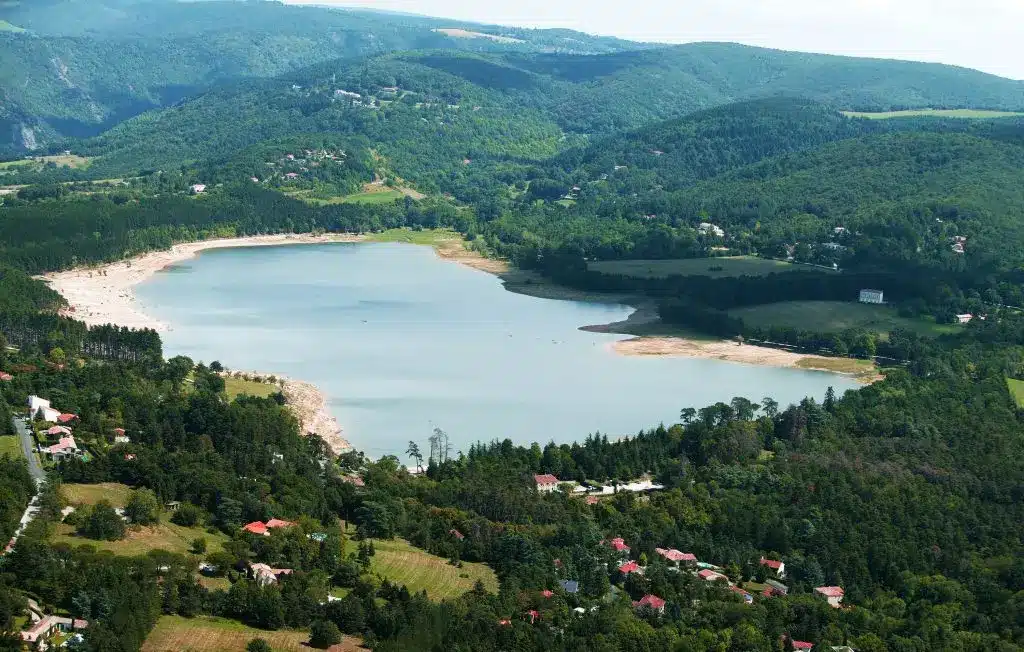 Superbe paysage de lac réservoir en montagne et forêt. Réservoir turquoise entouré de collines boisées. Le niveau d'eau bas expose la large plage bordée de maisons et de forêts.