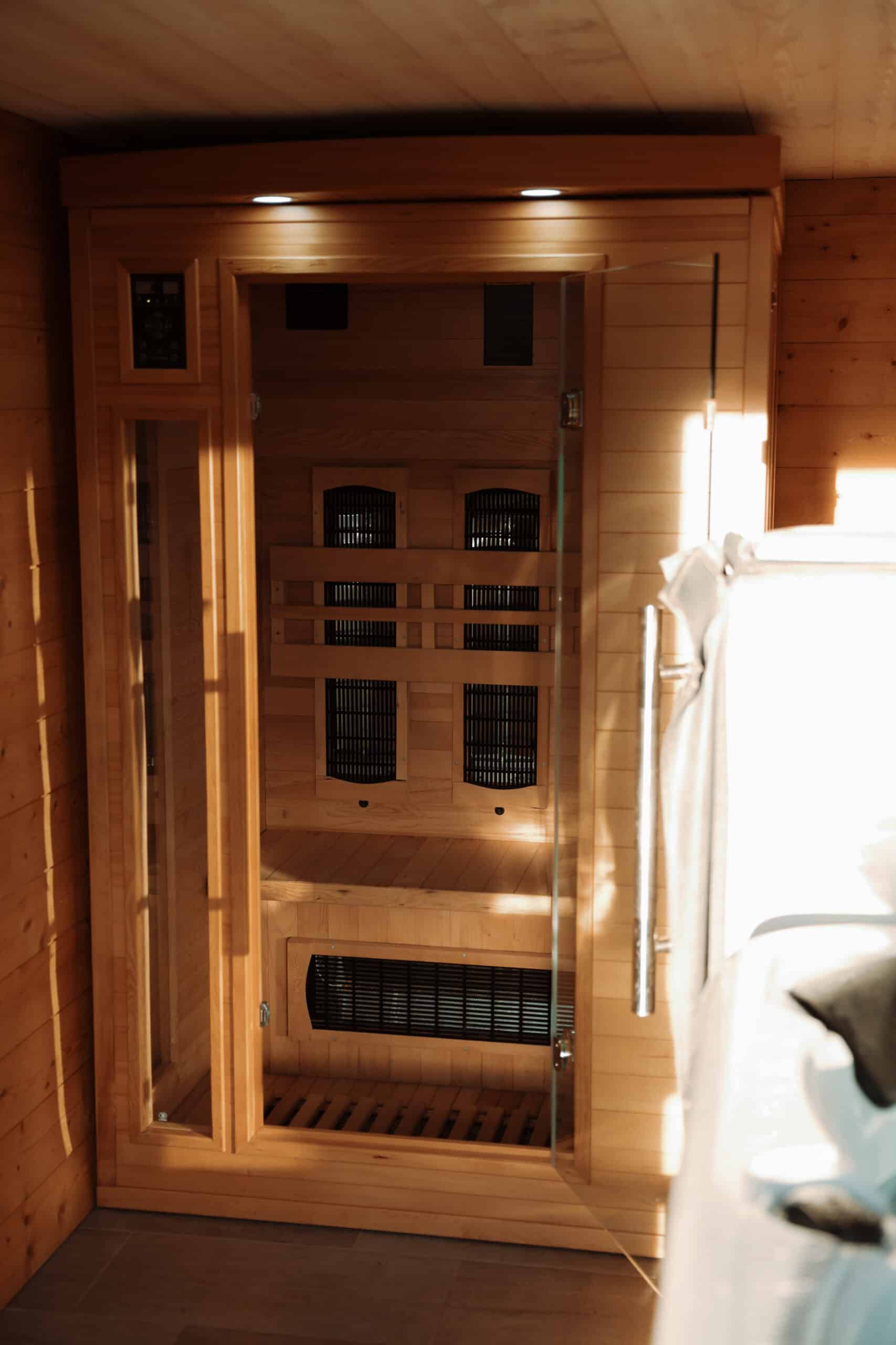 Sauna infrarouge en bois clair avec porte en verre. Lumière chaude du soleil frappant l'intérieur et l'environnement lambrissé du spa.