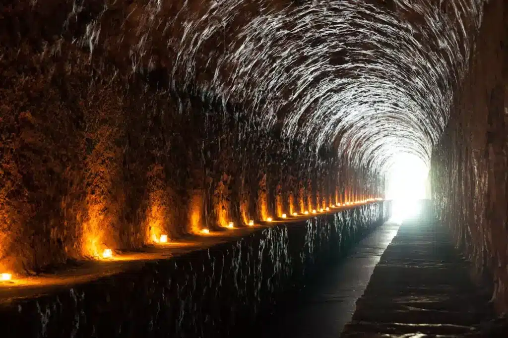 Mystérieux tunnel rocheux éclairé par des bougies chaudes Long tunnel rocheux voûté. Des bougies oranges jalonnent la paroi gauche, menant vers une intense lumière à l'extrémité.